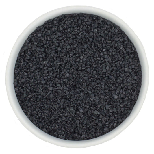 Top-down view of a white bowl filled with black coarse sanding sugar crystals, showing chunky dark granules and a dramatic charcoal-black color.