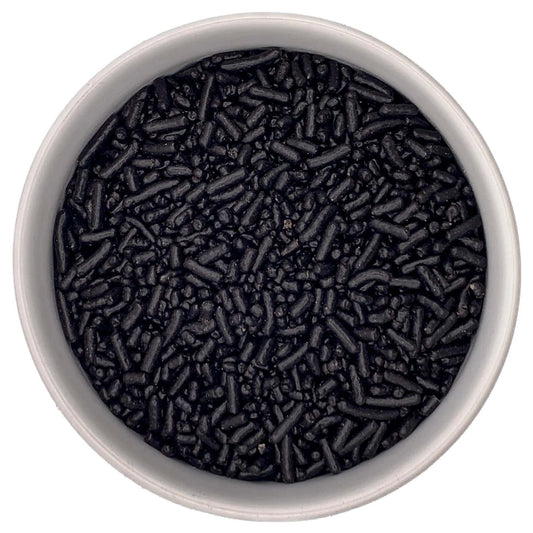 Overhead view of a white bowl filled with black jimmies sprinkles, showing small rod-shaped pieces and tiny bits clustered together.