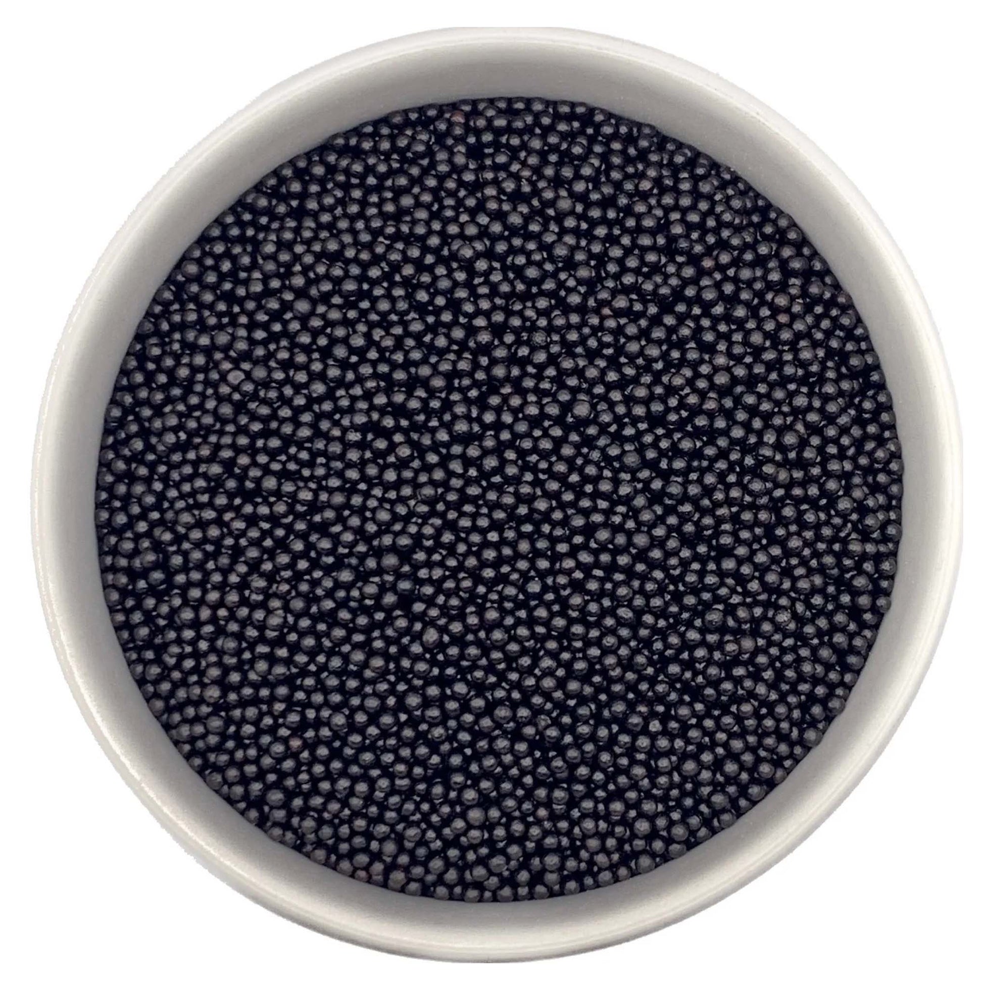 Top-down view of a white bowl filled with black non-pareils, showing tiny round sprinkle beads in a deep charcoal-black shade.