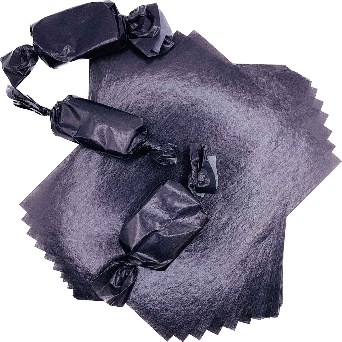 Three rectangular caramel pieces individually packaged in black wax candy wrappers with twisted ends, arranged over a stack of 4" x 5" caramel wrapper sheets.