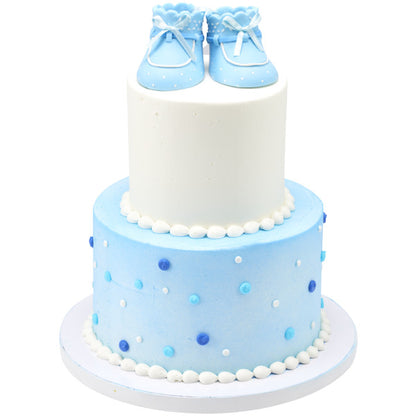 Two-tiered cake with white and blue frosting, topped with the blue baby booties cake decoration