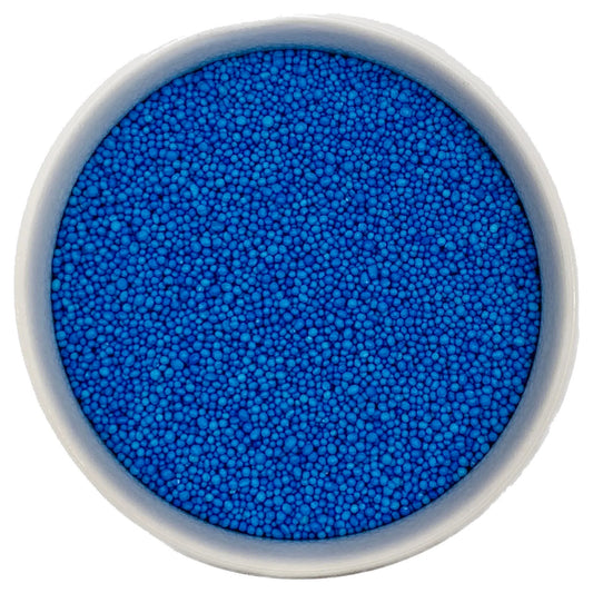 Top-down view of a white bowl filled with blue non-pareils, showing tiny round sprinkle beads in a vivid bright blue shade.