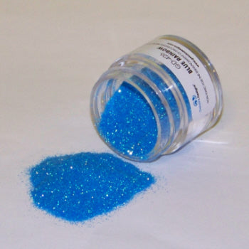 Small jar of bright blue Galaxy Glitter Dust labeled "Blue Rainbow," spilled onto a white surface, showcasing its vibrant shimmer.