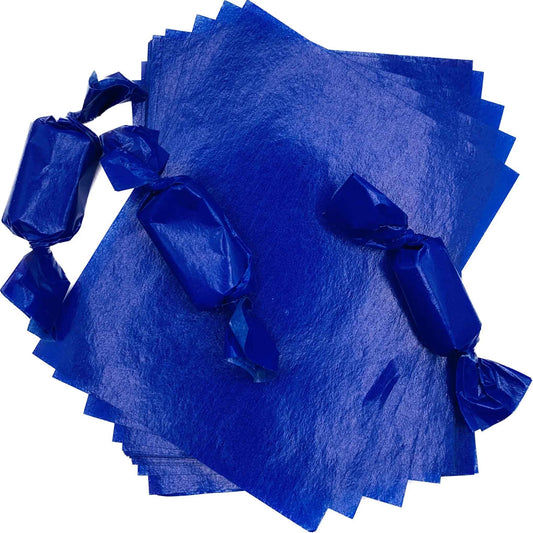Three rectangular caramel pieces individually packaged in deep blue wax candy wrappers with twisted ends, arranged over a stack of 4" x 5" caramel wrapper sheets.