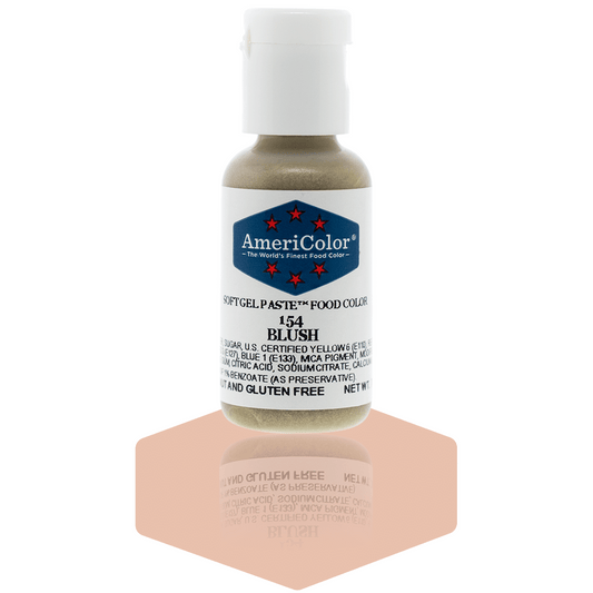 A bottle of AmeriColor Blush soft gel paste food coloring with a white cap, blue label, and red stars, standing on a soft blush pink reflective surface that mirrors the bottle.