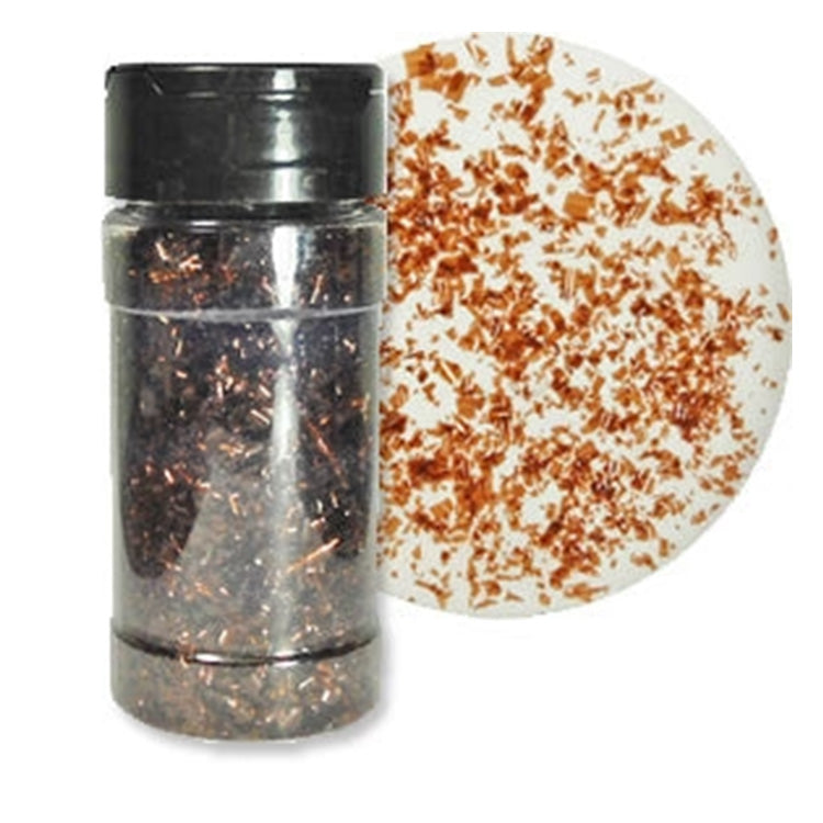 Clear shaker bottle filled with brown edible glitter flakes beside a white round surface scattered with warm copper-brown shimmering flakes.