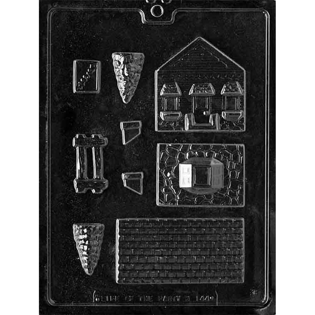 Clear plastic chocolate mold with small house building panel cavities, including a roof piece with shingle texture, wall sections with window outlines, and additional small components for assembling a 3D house.