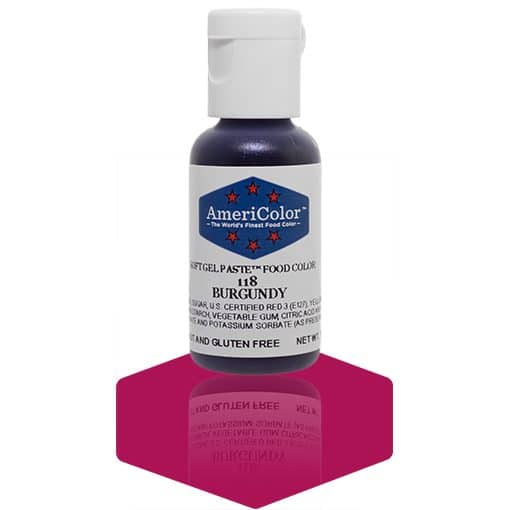 A bottle of AmeriColor Burgundy soft gel paste food coloring, featuring a white cap and blue label with red stars, positioned on a dark burgundy reflective surface with the bottle’s reflection visible.