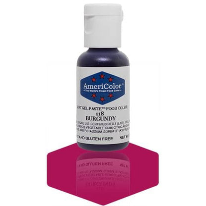 A bottle of AmeriColor Burgundy soft gel paste food coloring, featuring a white cap and blue label with red stars, positioned on a dark burgundy reflective surface with the bottle’s reflection visible.