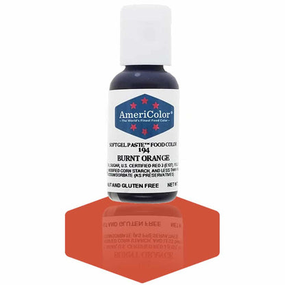 A bottle of AmeriColor Burnt Orange soft gel paste food coloring with a white cap and blue label featuring red stars, standing on a deep burnt orange reflective surface that mirrors the bottle.