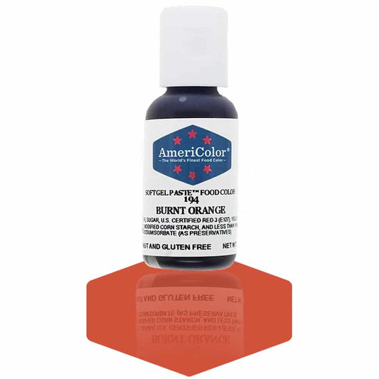 A bottle of AmeriColor Burnt Orange soft gel paste food coloring with a white cap and blue label featuring red stars, standing on a deep burnt orange reflective surface that mirrors the bottle.
