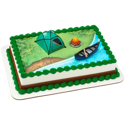 Campfire, tent, and canoe decorations on a sheet cake with a printed forest and river scene and green icing border