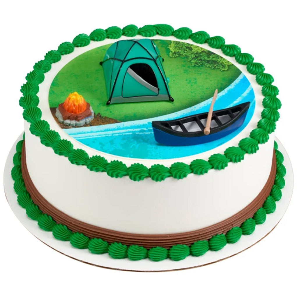 Tent, campfire, canoe, and paddle decorations on a round white cake with a printed campsite scene and green icing borders