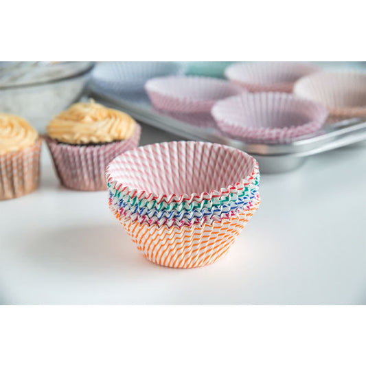 Stack of multicolored striped cupcake liners on a kitchen counter near baked cupcakes and a muffin pan.