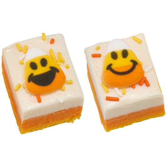 Two frosted Halloween dessert bars topped with candy corn face sugar decorations and orange and yellow sprinkles.