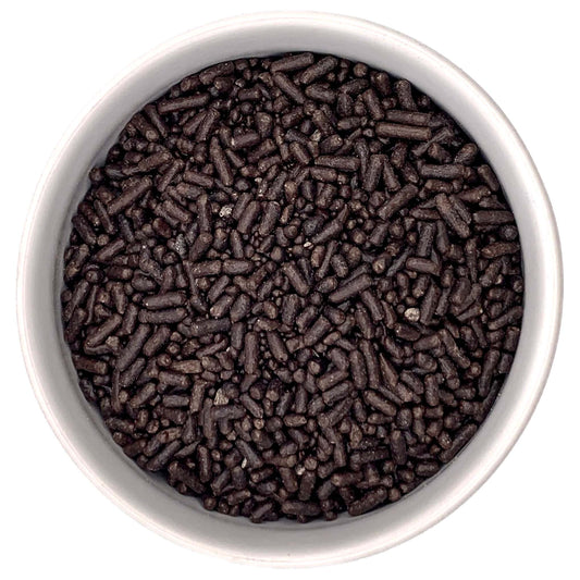 Top-down view of a white bowl filled with dark brown chocolate jimmies sprinkles, showing short rod-shaped pieces and small sprinkle bits.
