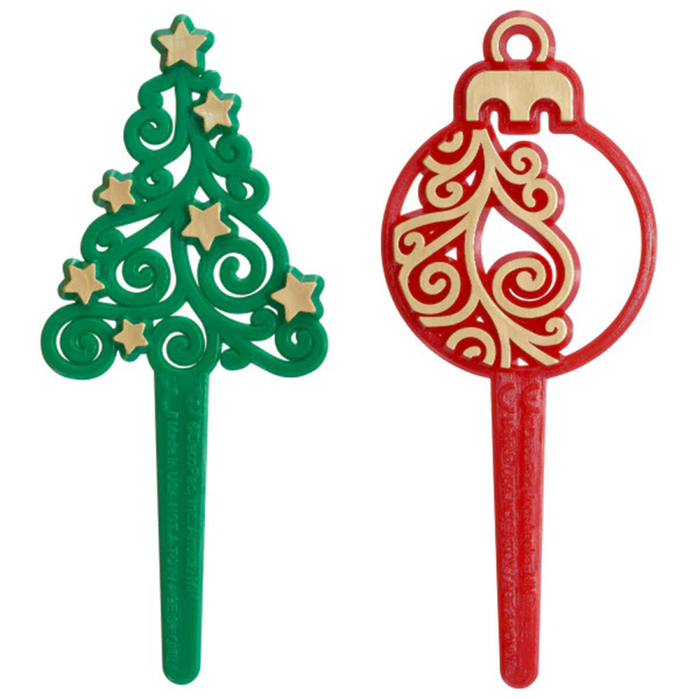 Green Christmas tree dessert pick with gold star accents and a red ornament dessert pick with gold swirl pattern, both shown on long plastic stakes against a white background.