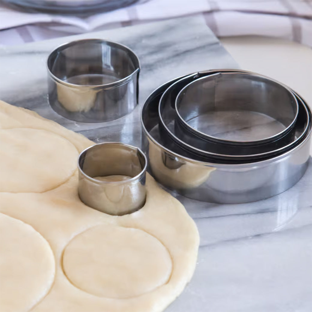 Circle cutter set in use, cutting round shapes from dough on a marble surface.