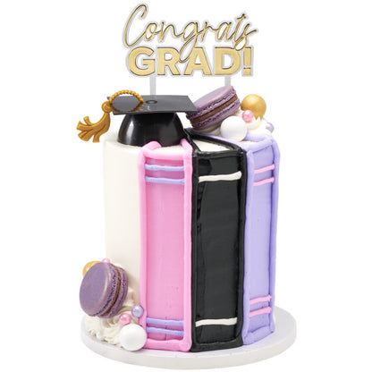 Vertical graduation cake shaped like textbooks, topped with graduation cap and "Congrats GRAD!" cake pick
