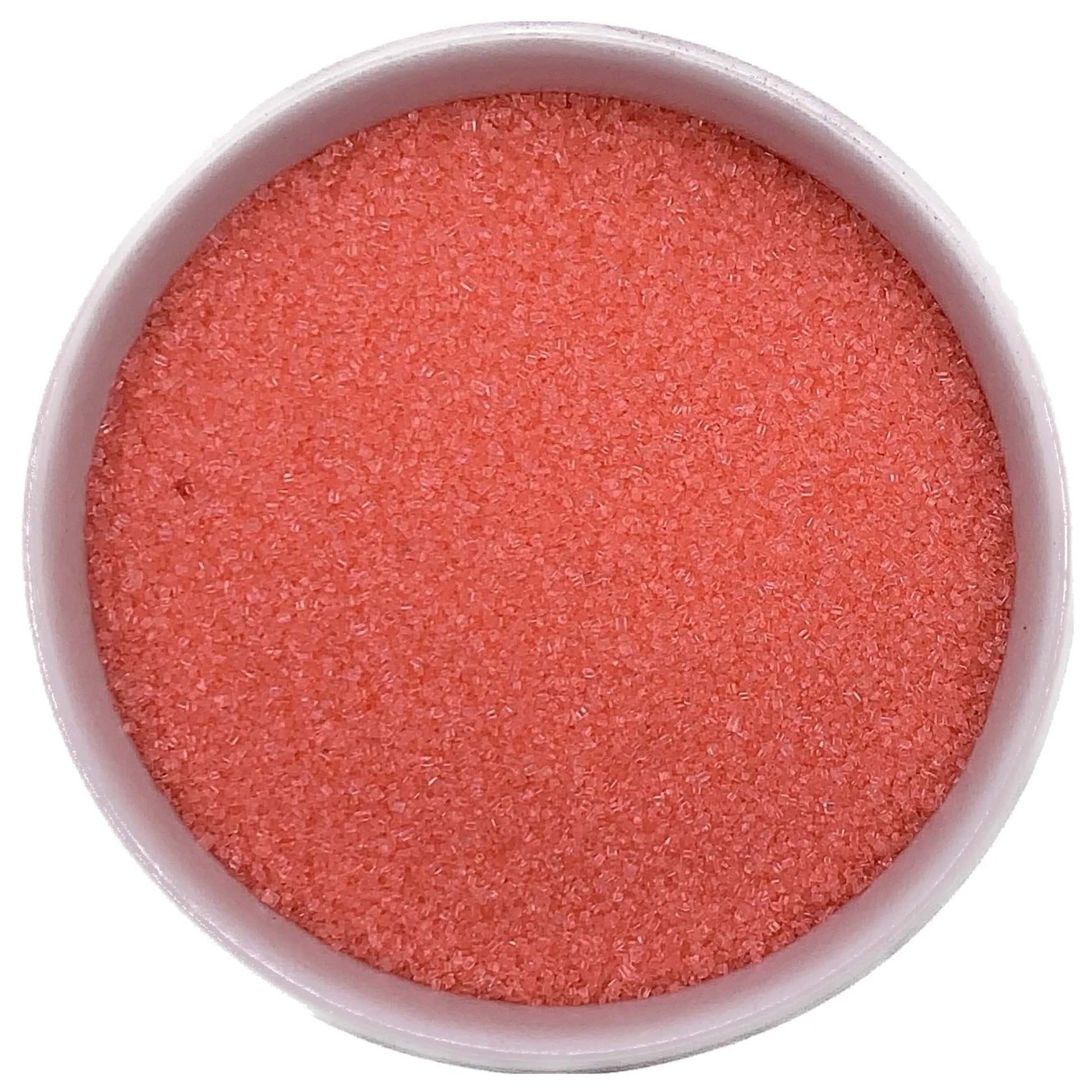 Top-down view of a white bowl filled with coral fine sanding sugar, showing tiny sparkling crystals in a soft orange-pink shade.