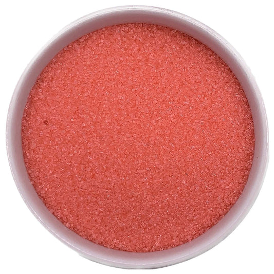 Top-down view of a white bowl filled with coral fine sanding sugar, showing tiny sparkling crystals in a soft orange-pink shade.