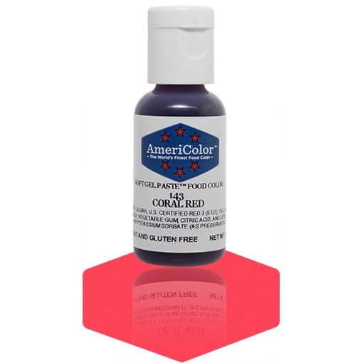 A bottle of AmeriColor Coral Red soft gel paste food coloring with a white cap, blue label, and red stars, positioned on a bright coral red reflective surface with the bottle’s reflection clearly visible.
