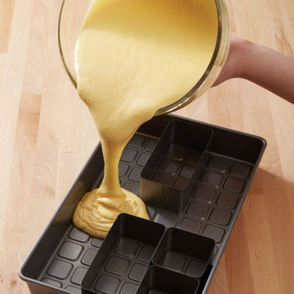 Yellow cake batter being poured into configured inserts inside the rectangular cake pan.