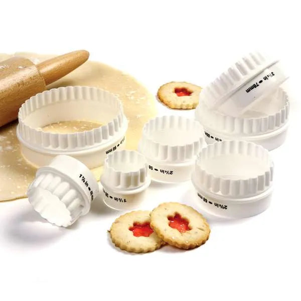 White, round, fluted cookie cutters with dough and cut cookies.