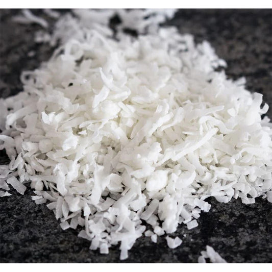 Close-up of desiccated coconut flakes on a dark surface, unsweetened and finely shredded for baking and cooking