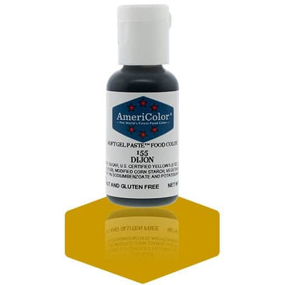 A bottle of AmeriColor Dijon soft gel paste food coloring with a white cap, blue label, and red stars, positioned on a mustard-yellow reflective surface with the bottle’s reflection clearly visible.