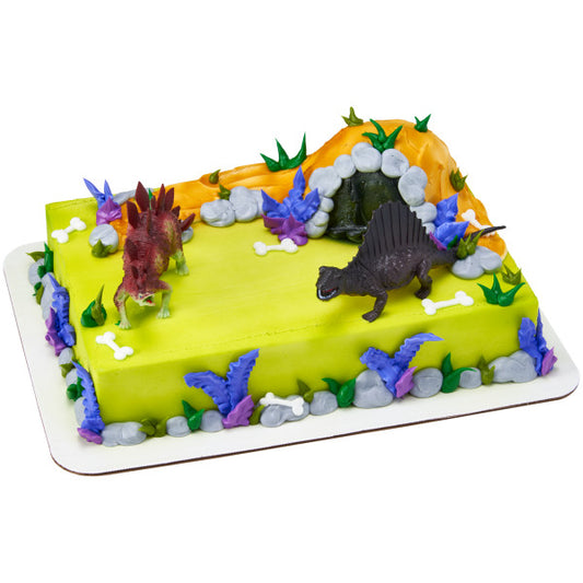 Sheet cake decorated with dinosaur toppers, foliage, and a rocky cave design featuring a Stegosaurus and Spinosaurus figurine.
