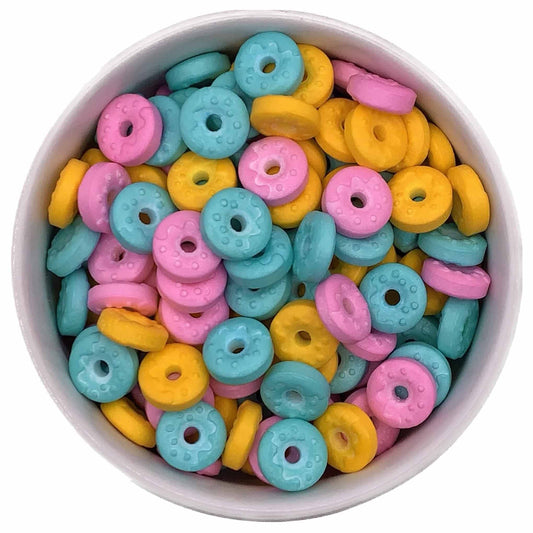 Bowl of pink, blue, and yellow donut-shaped sprinkles with center holes and raised icing designs