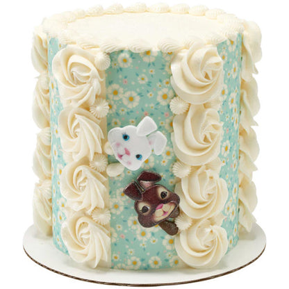 Tall Easter cake decorated with blue floral panels, white buttercream rosettes, and white and brown bunny face rings arranged on the front.