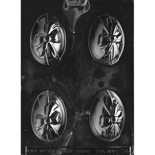 Clear plastic chocolate mold with four single-sided egg cavities, each featuring a raised ribbon and bow design across the front of the egg, shown on a dark background.