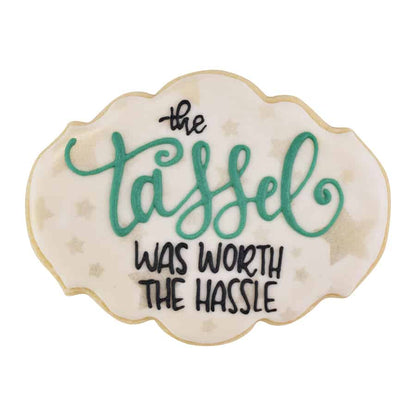 Graduation-themed cookie with the message "The tassel was worth the hassle" in green and black icing.