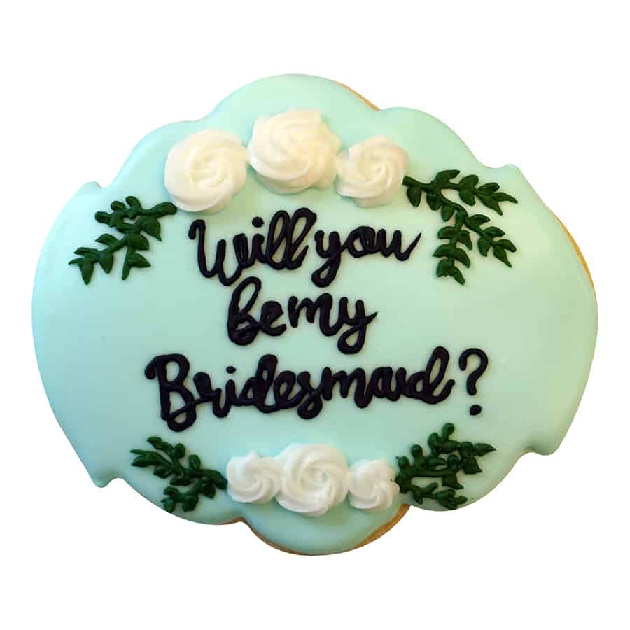 Light blue iced cookie with piped message "Will you be my bridesmaid?" and floral details.