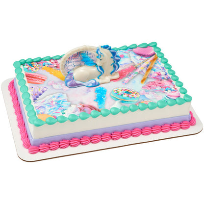 Rectangular cake with whimsical candy-themed graphics, topped by an enchanting unicorn figurine cake decoration, bordered with pastel pink, purple, and turquoise icing.