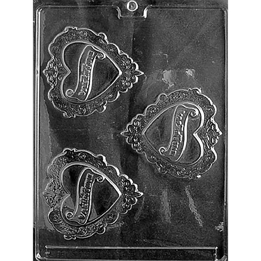 Clear plastic chocolate mold photographed on a black background with three ornate heart-shaped cavities featuring raised decorative borders and a large scripted letter in the center.