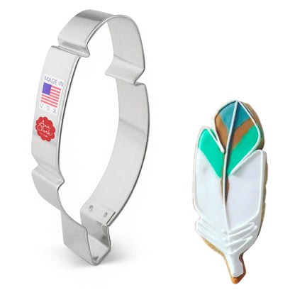 Metal feather cookie cutter next to a decorated sugar cookie shaped like a feather, featuring white, teal, and brown icing.