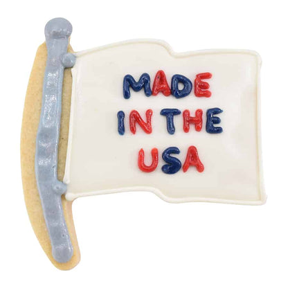 Flag-shaped cookie decorated with 'Made in the USA' text in red and blue icing on a white background.