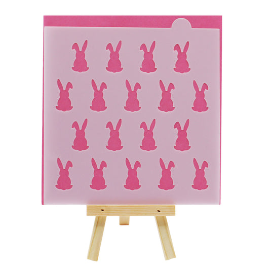 Floppy ear bunny cookie and cake stencil with repeating rabbit silhouettes, displayed in translucent plastic against a pink background on a small wooden easel.