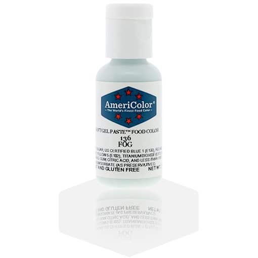 A bottle of AmeriColor Fog soft gel paste food coloring with a white cap, blue label, and red stars, positioned on a light fog gray reflective surface with the bottle’s reflection clearly visible.