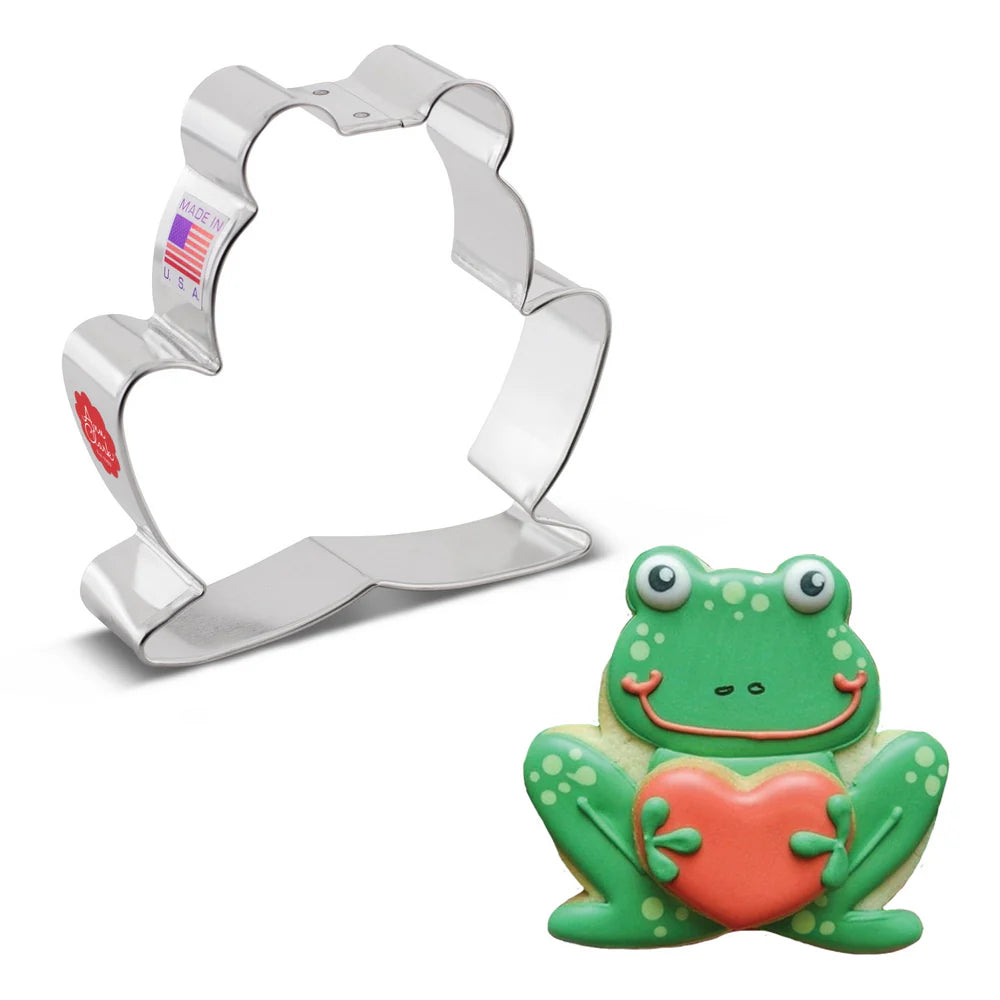 Frog cookie cutter alongside a decorated green frog cookie holding a red heart.