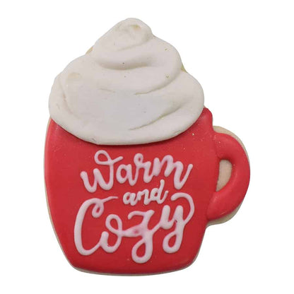 Decorated cookie shaped like a red mug with "Warm and Cozy" written in white icing, topped with fluffy whipped cream.