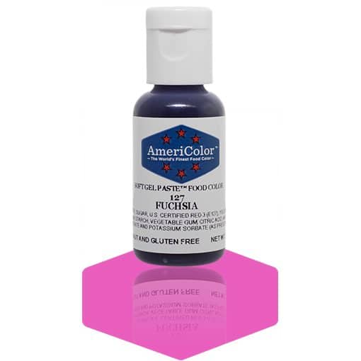 A bottle of AmeriColor Fuchsia soft gel paste food coloring with a white cap and blue label adorned with red stars, standing on a vibrant pink reflective surface with the bottle’s reflection visible.