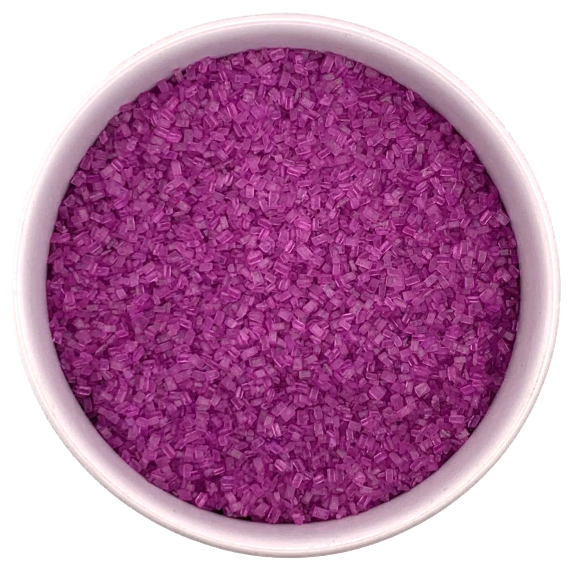 Top-down view of a white bowl filled with fuchsia coarse sanding sugar crystals, showing vivid magenta-purple chunky granules packed closely together.