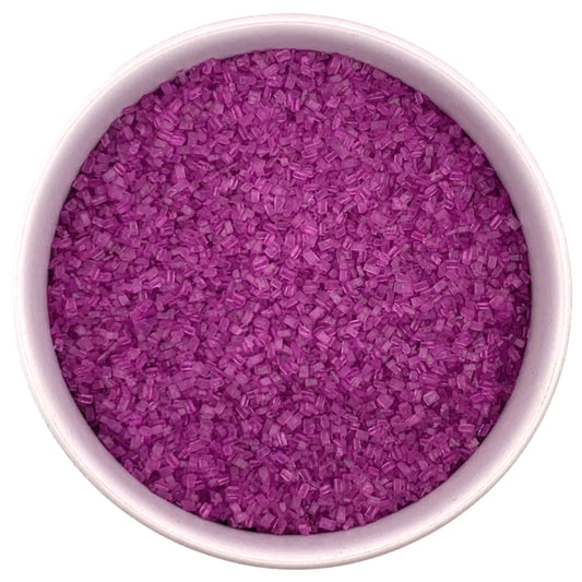Top-down view of a white bowl filled with fuchsia coarse sanding sugar crystals, showing vivid magenta-purple chunky granules packed closely together.