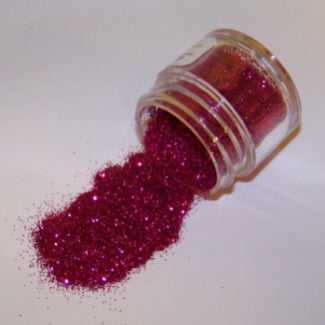 Jar of fuchsia raspberry-toned Galaxy Glitter Dust tipped over, spilling a vivid magenta-red shimmer across a white surface.