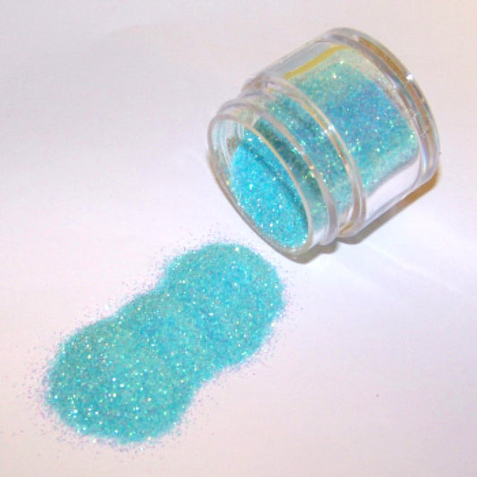 Small jar tipped on its side spilling aqua blue glitter dust onto a white surface.