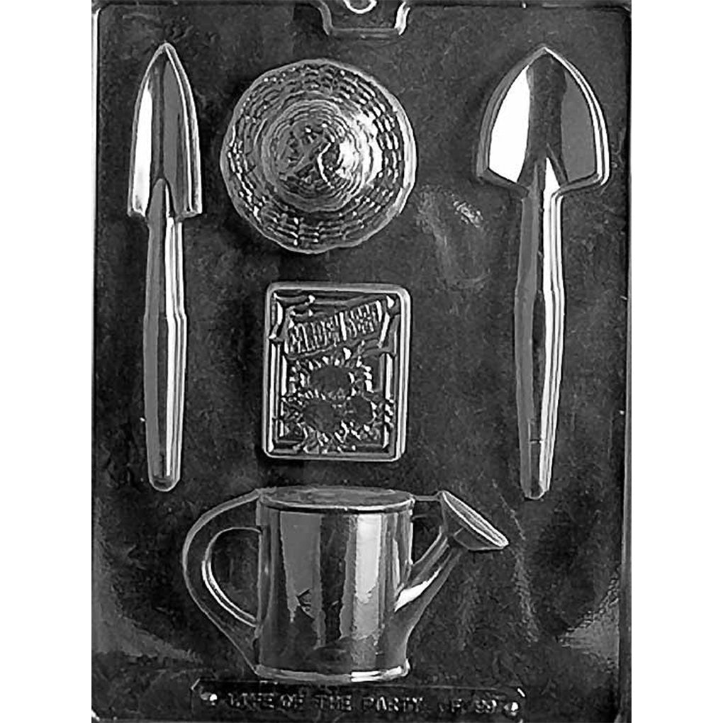 Clear plastic chocolate mold showing assorted gardening-themed cavities, including a watering can, two garden trowels, a round textured piece, and a small rectangular design, on a dark background.